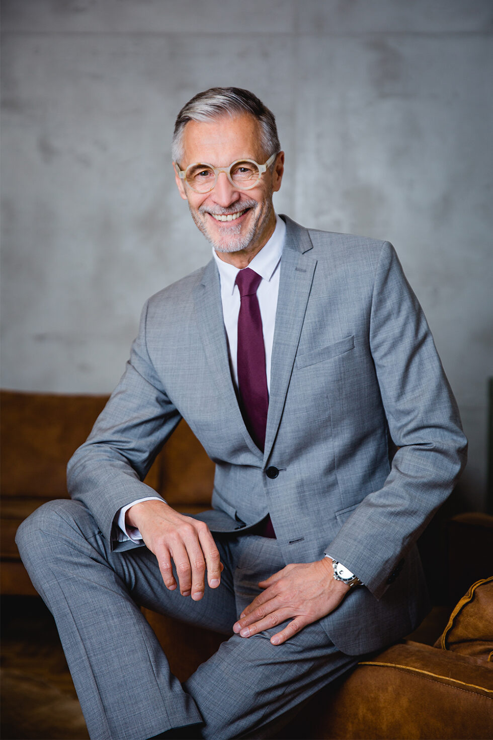 Businessportrait eines grauhaarigen Mannes in einem grauen Anzug mit dunkelroter Krawatte