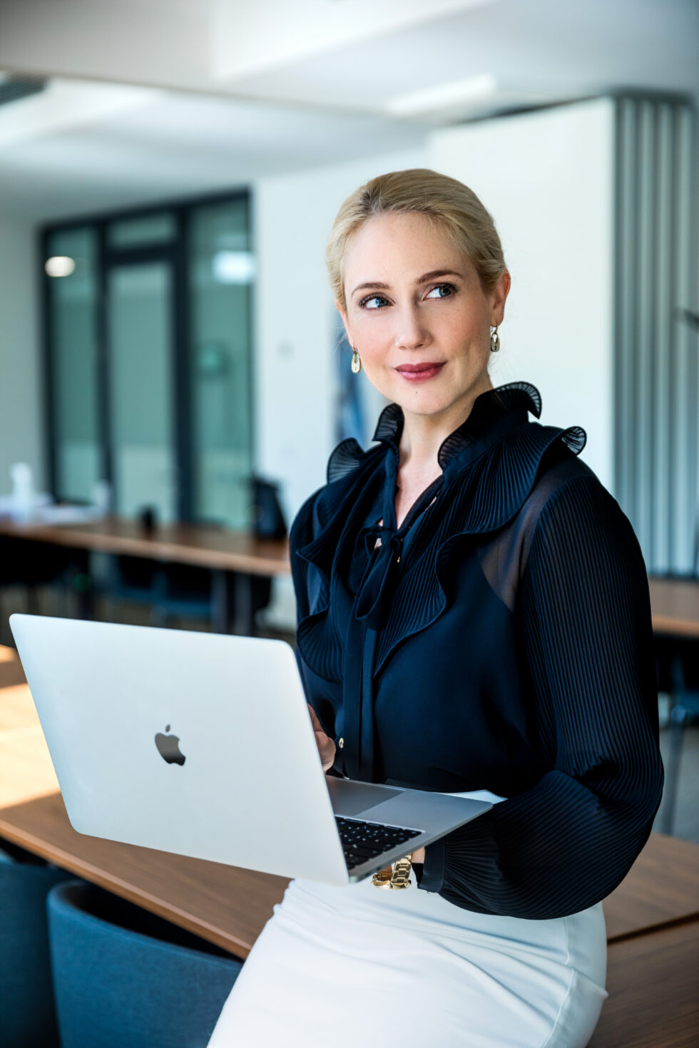 Eine blonde Frau mit einem MacBook in der Hand und Business Kleidung