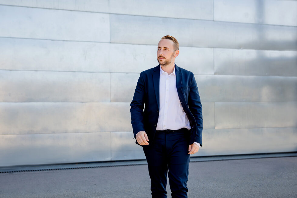 modernes Bewerbungsfoto von einem Mann mit blauen Anzug, der vor einem silbernen Tor läuft