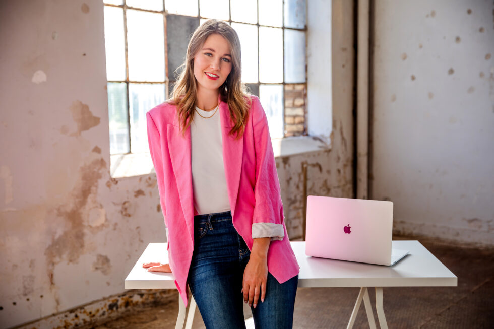 Business Foto einer Frau mit pinken Blazer vor einem Schreibtisch mit MacBook