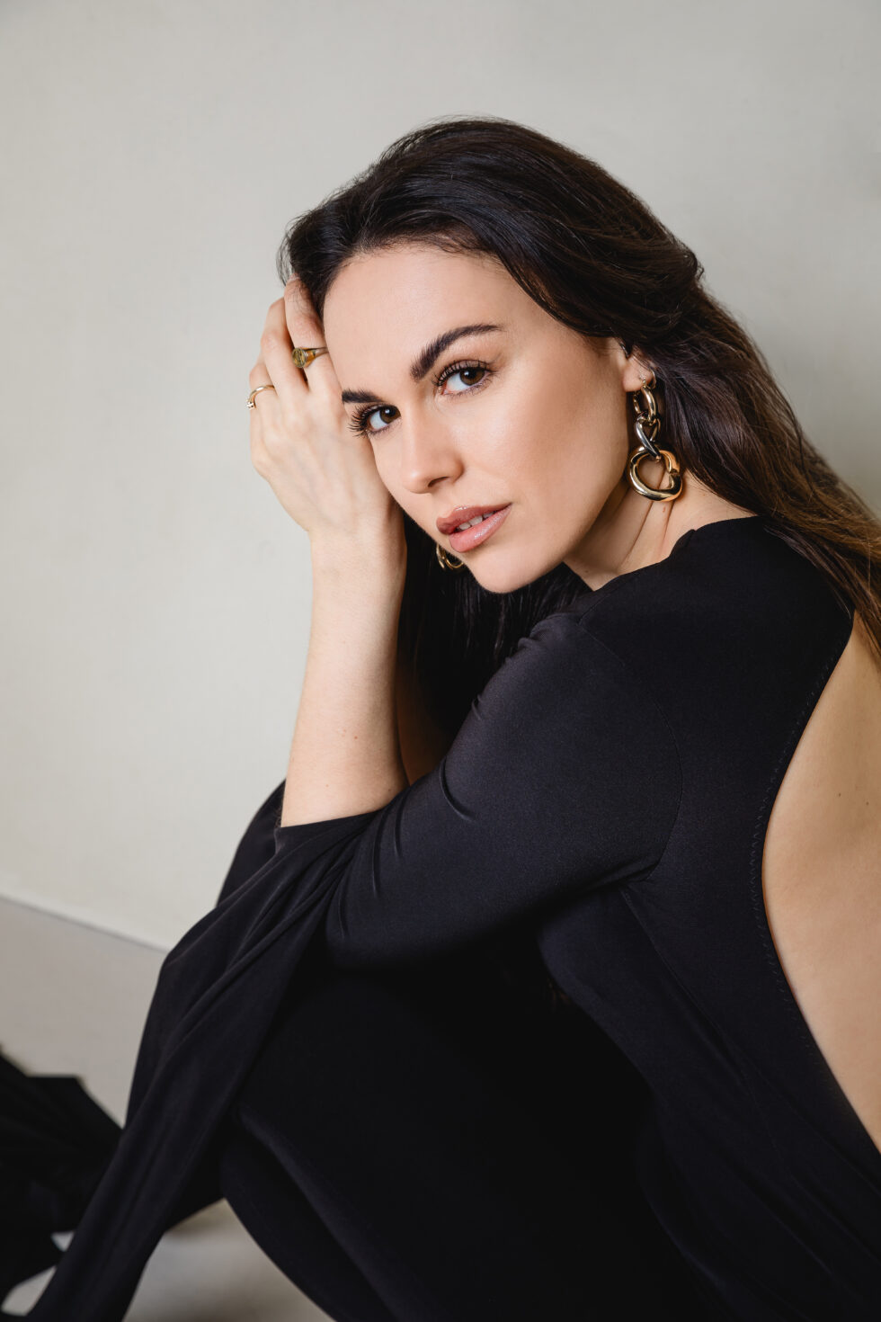 Portrait einer sitzenden Frau, die in die Kamera schaut. Sie trägt einen schwarzen jumpsuit.