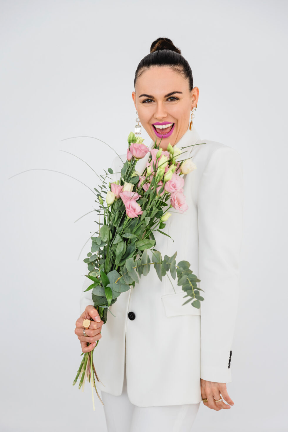 Portrait einer Frau in weißer Kleidung mit einem Blumenstrauß in der Hand, die in die Kamera lacht