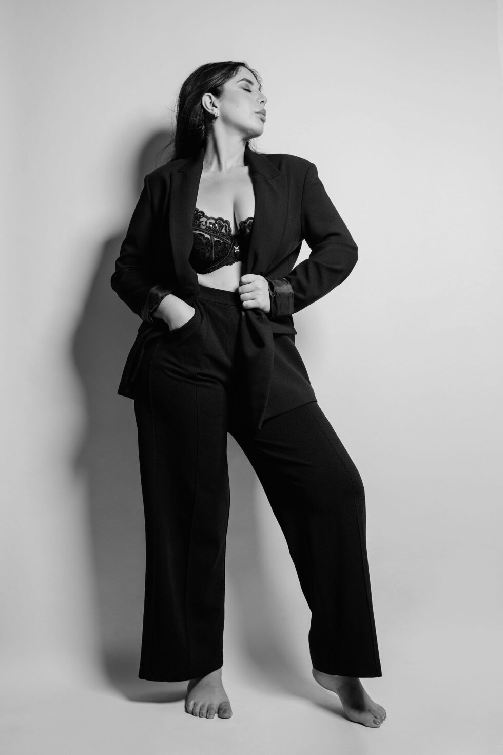 Schwarz-weiß Foto einer Frau in BH und Blazer, sie steht vor einer weißen Wand