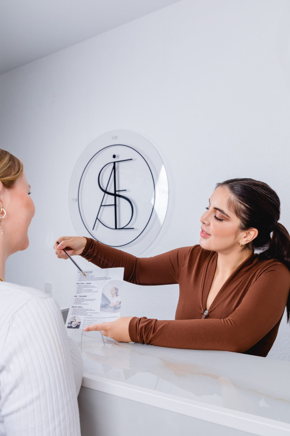 Die Mitarbeiterin zeigt einer Kundin etwas auf einem Flyer