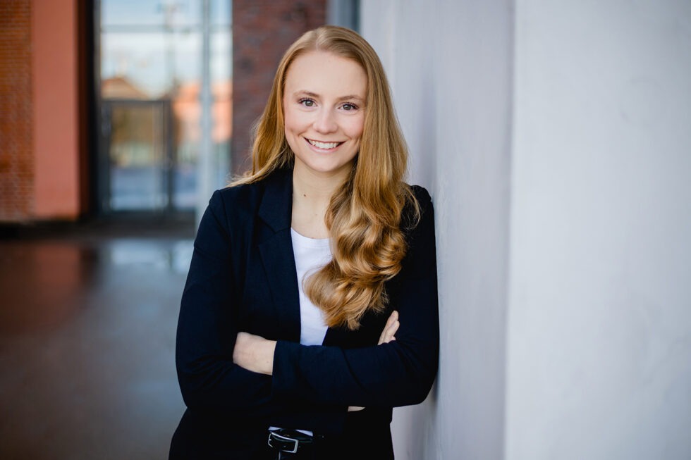 modernes Bewerbungsfoto einer rothaarigen jungen Frau mit schwarzem Blazer mit verschränkten Armen