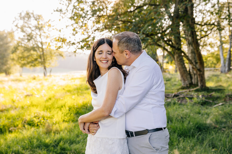 Ein Mann küsst seine Partnerin auf die Backe. Sie stehen in der Natur.