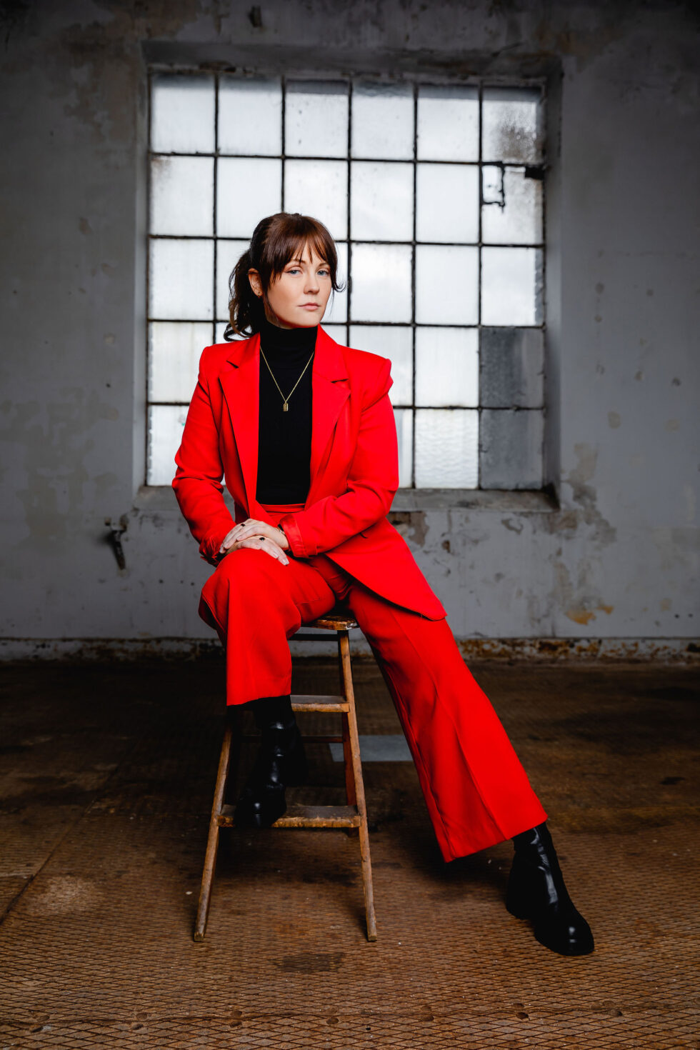 eine Frau in einem roten. Anzug sitzt auf einem Hocker in einer Industriehalle